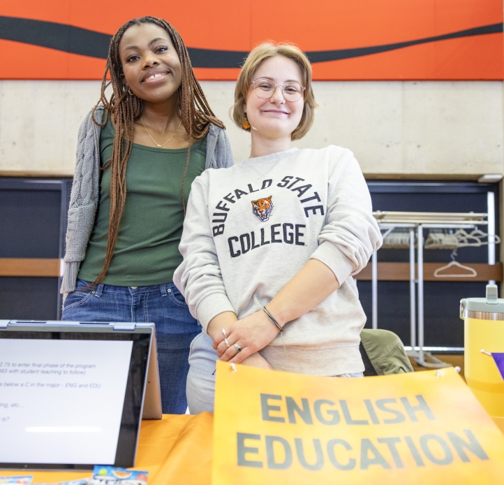 two students behind English Education table smiling at camera