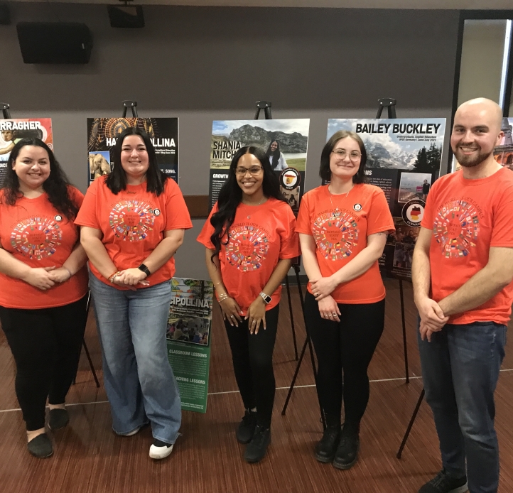 five students in orange tshirts posing by their posters