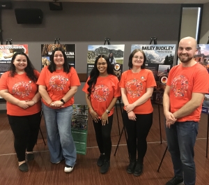 five students in orange tshirts posing by their posters